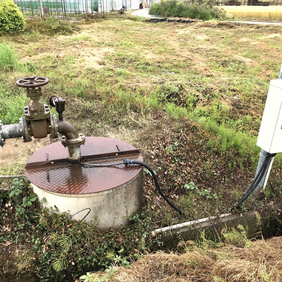 Tapa de un pozo con tubería de bombeo y válvula en una zona agrícola