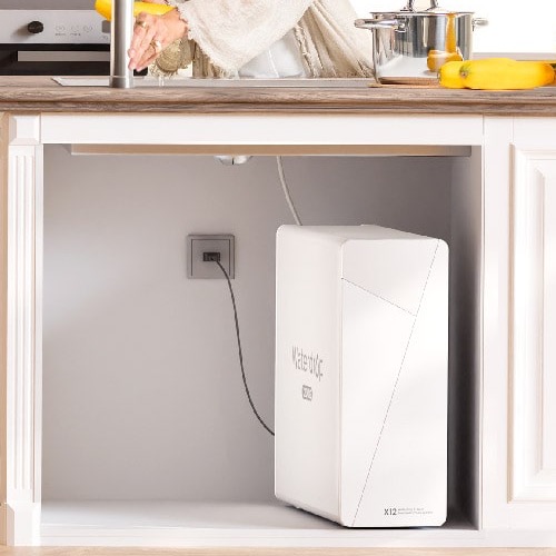 Waterdrop X12 dentro de un mueble abierto bajo el fregadero, junto a un enchufe